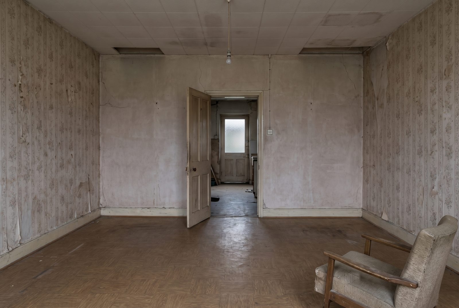 Avant les travaux&nbsp;: un mur porteur plâtré percé d’une porte étroite, papier peint fleuri décollé, faux plafond taché, linoléum brun.