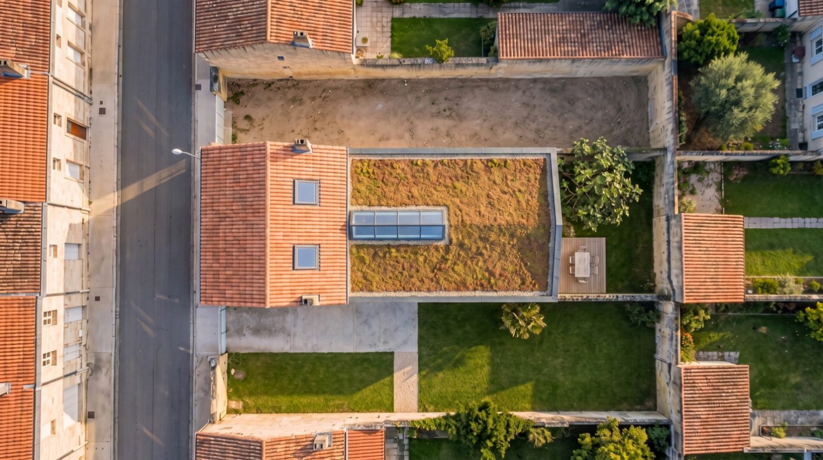Après les travaux, vue du ciel : toit de tuiles neuf à fenêtres de toit, extension sous toit végétalisé et sa verrière, terrasse, pelouse et figuier.
