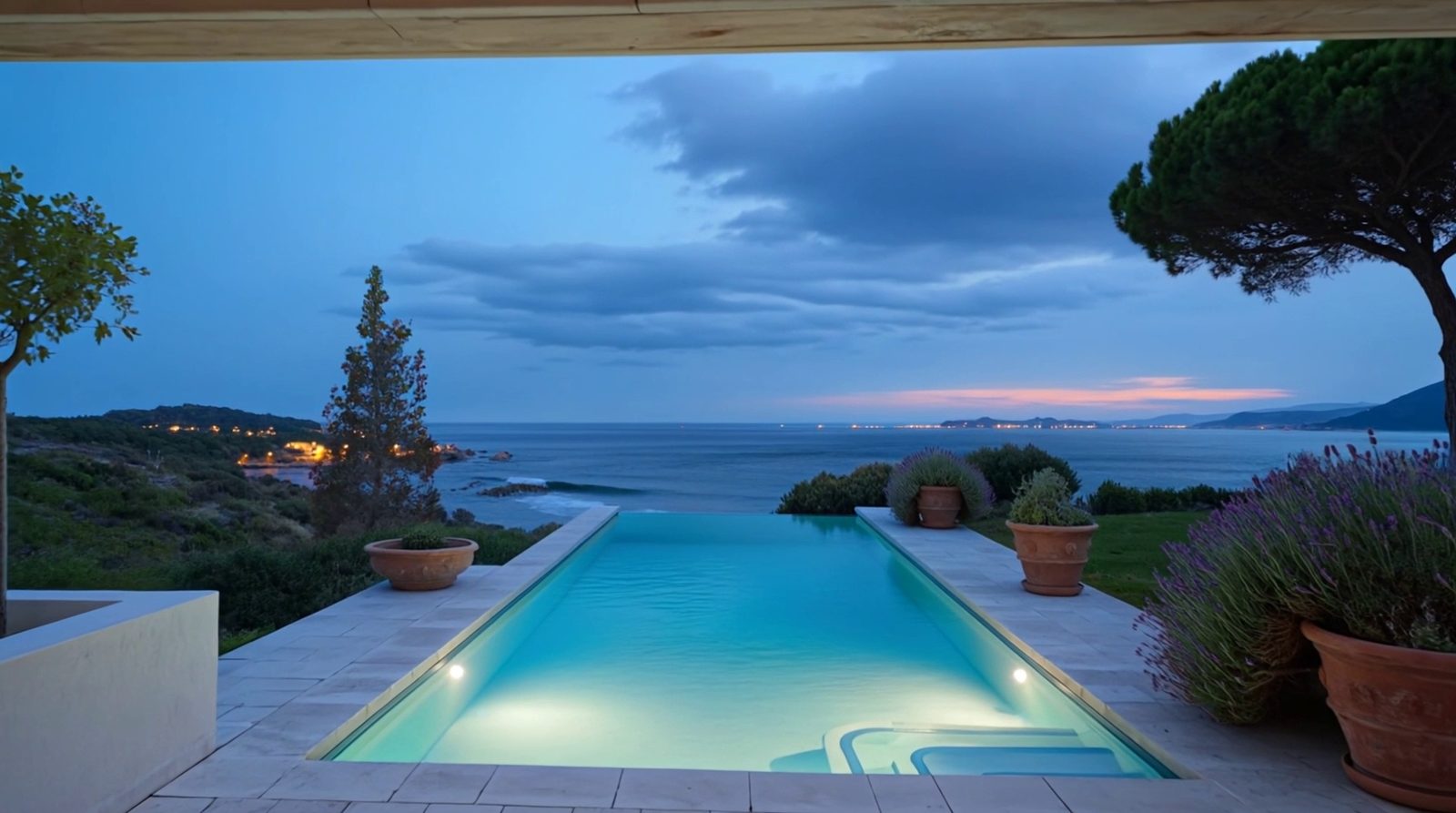 Au bord de la piscine, la mer et la côte éclairée à l’heure bleue.